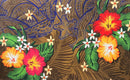 A flat-lay view of the Hibiscus, Plumeria Assortment Sarong (Style 11) featuring a vibrant Polynesian-inspired design. The pattern includes large hibiscus flowers in gradients of red, orange, and yellow, mixed with white and pink plumeria blossoms. The background features a mix of earthy brown and deep blue sections adorned with traditional Polynesian tribal motifs, tattoo-inspired geometric patterns, and lush green monstera and palm leaves.