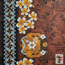 A close-up of a brown tropical fabric or wallpaper pattern featuring plumeria flowers, monstera leaves, a tribal geometric border on the left, and a central crest emblem.