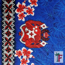 Blue fabric featuring a red and white Tonga coat of arms, red and white plumeria flowers, a black, red, and white geometric border on the left, and blue tropical leaf patterns.